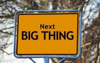 A yellow road sign that says, “Next big thing,” framed by a blue metal tube.