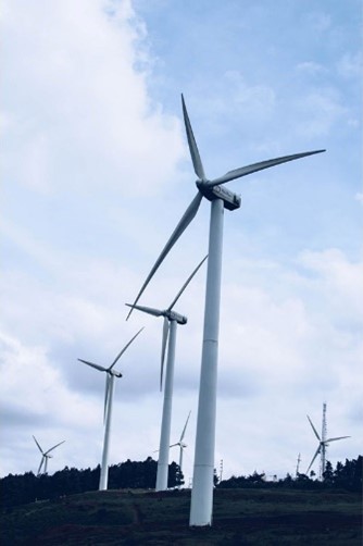 A picture of an array of white wind turbines across a land under the sky of a blue and cloudy sky.