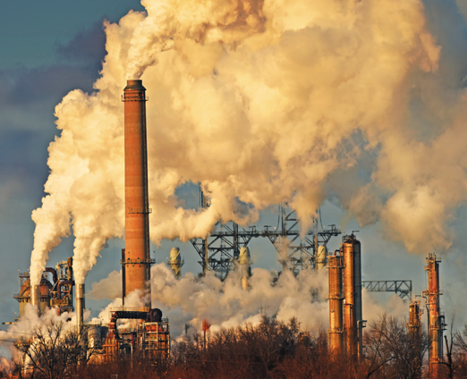 A fossil fuel production plant—orange towers with plumes of smoke pouring out, an electrical grid in the background, against a blue sky.