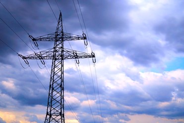 A beautiful angle of a very large electrical power transformer majestically positioned against a cloudy sky as the sun sets, casting various hues of turquoise, yellow, orange, and red around the white clouds.