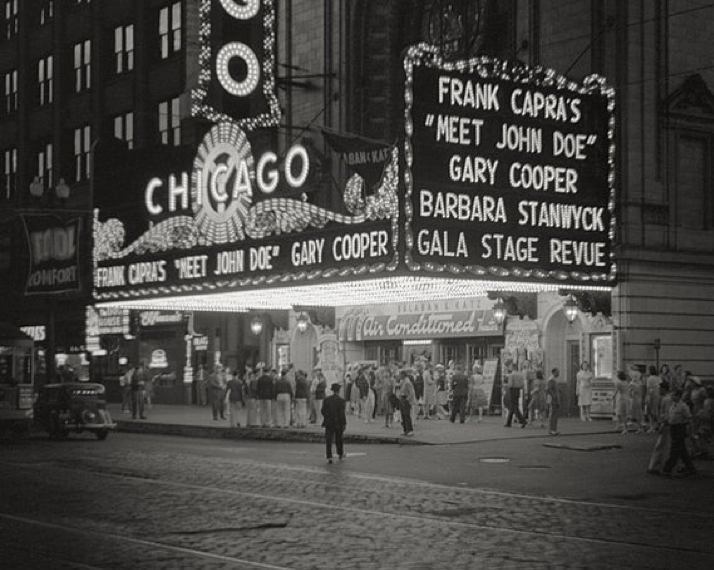 A black and white picture of The Chicago Theater at night, with a lit-up marquee that reads: “Frank Capra’s ‘Meet John Doe’ Gary Cooper, Barbara Stanwyck, Gala Stage Revue. (1941)