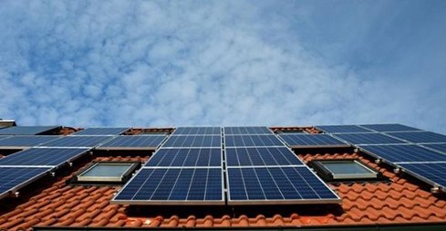 A picture of a terra cotta roof with blue and white solar panels, skylights, and a cloudy sky above.