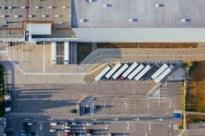 A birds-eye view of a large factory, a large parking lot, and trucks lined up in front waiting to be loaded at the docking bays or in long parking spaces.
