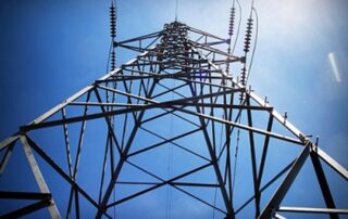 A close-up photograph of a power line tower from the ground looking skyward.